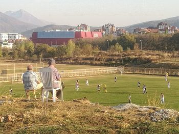 People on field by buildings against sky