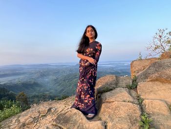 Young woman standing on rock against sky