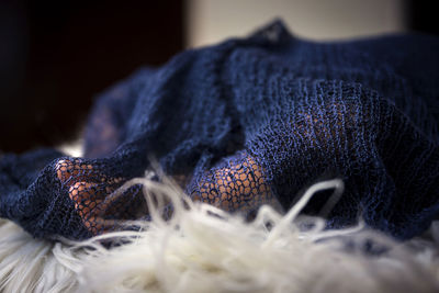 Close-up of person under knitted blanket on bed