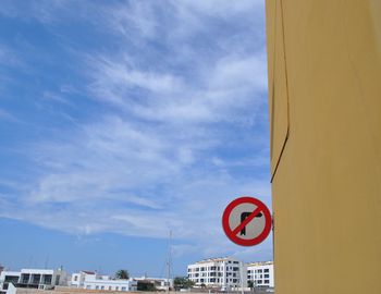 Low angle view of road sign by buildings against sky