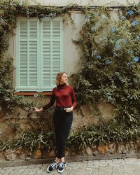 Full length portrait of young woman standing against building