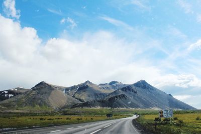 Country road leading towards mountains against sky