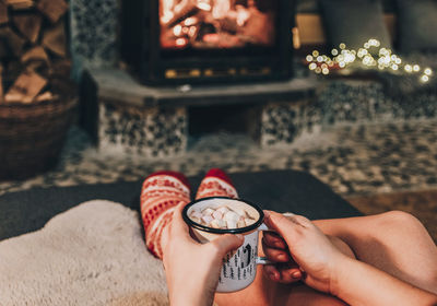 Personal perspective of woman relaxing on sofa by fireplace. holding cocoa.