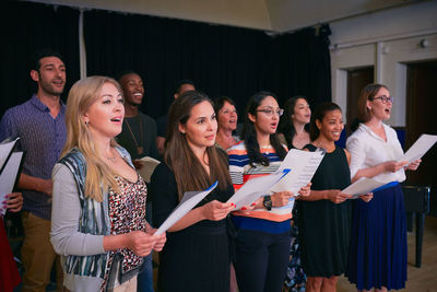 Male and female friends practicing choir on stage in auditorium