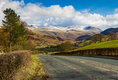 Road amidst trees and mountains against sky