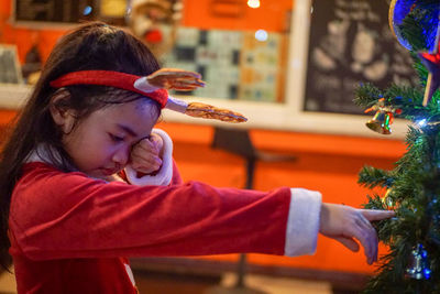 Sad girl in costume pointing at christmas tree