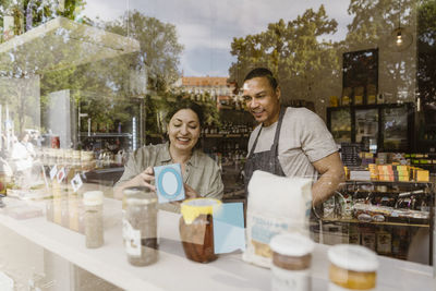 Happy owners discussing over merchandise in store seen through glass