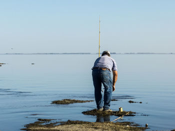 Man fishing in sea against clear blue sky