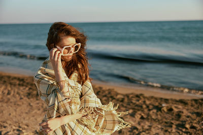 Young woman drinking water while standing at beach