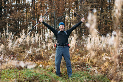 Portrait of happy mature man with trekking poles in autumn forest