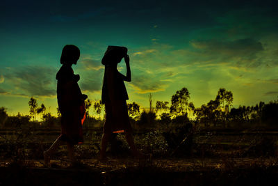 Silhouette people standing on field against sky during sunset