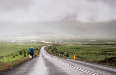 Rear view of person biking on country road along landscape