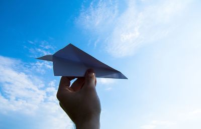 Low angle view of person holding paper plane against sky