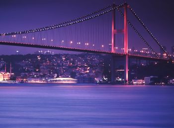 Low angle view of illuminated bosphorus bridge over river against cityscape
