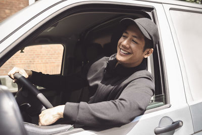 Smiling delivery man looking through window while sitting in truck