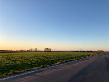 Road by agricultural field against clear sky
