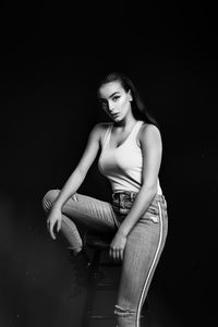 Portrait of woman sitting against black background