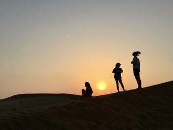 Silhouette people on desert against sky during sunset