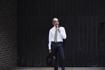 Portrait of stylish senior businessman with grey hair standing against dark background