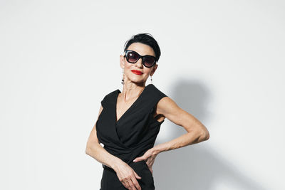 Portrait of young woman wearing sunglasses while standing against white background