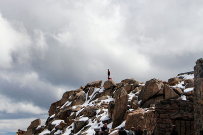 Man standing on snow covered rocks against cloudy sky