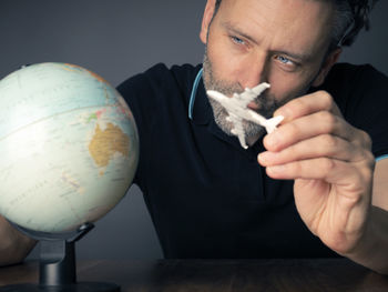 Mature man holding model airplane with globe on table