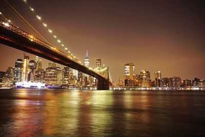 Illuminated bridge over river by buildings against sky at night