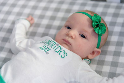 Close-up portrait of cute baby girl wearing green headband lying on bed at home