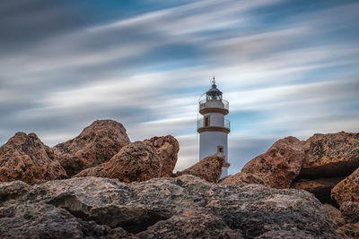 Lighthouse on rock by sea against sky