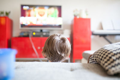 Rear view of boy watching tv in living room at home