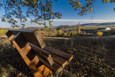 Empty bench on field by trees against sky