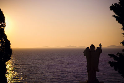 Silhouette statue at beach against clear sky during sunset