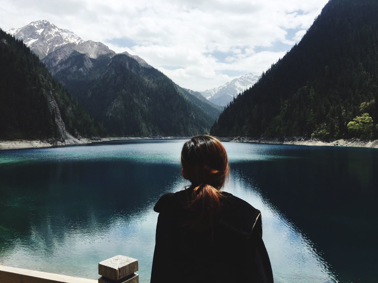 mountain, rear view, water, lake, nature, one person, real people, beauty in nature, scenics, day, tranquility, mountain range, sky, leisure activity, standing, outdoors, young adult, lifestyles, young women, tree, people