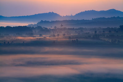 Scenic view of silhouette landscape during foggy weather at sunset