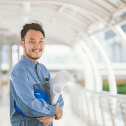 Portrait of smiling engineer with blueprints standing on footbridge