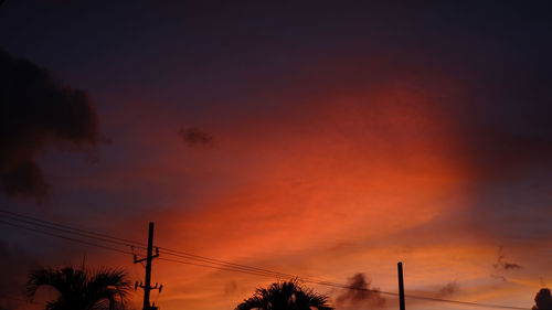 Low angle view of silhouette electricity pylon against dramatic sky