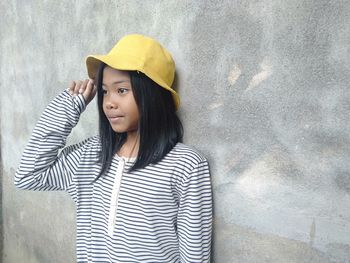 Close-up of cute girl wearing hat standing against wall