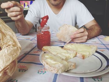 Midsection of man eating bread with preserves at table