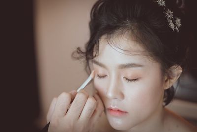 Cropped hand of person doing makeup of young woman at home