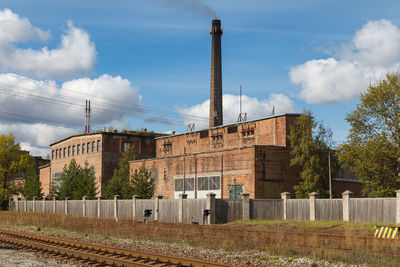 Factory by railroad tracks against sky