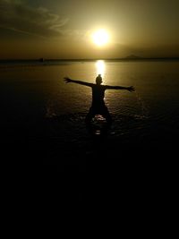 Silhouette man standing in sea against sky during sunset