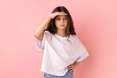 Portrait of young woman standing against pink background