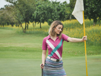 Young woman holding umbrella while standing on golf course