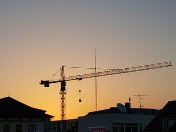 Low angle view of silhouette crane by building against sky during sunset