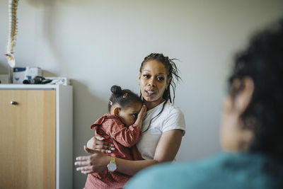 Woman carrying ill daughter discussing with doctor in clinic