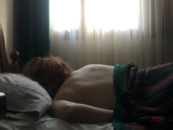 Rear view of boy sleeping on bed