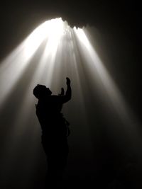 Low angle view of silhouette man standing with arms raised in dark cave