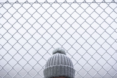 View of person head wearing knit hat standing by chainlink fence