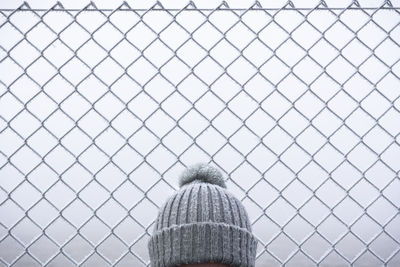 View of person head wearing knit hat standing by chainlink fence