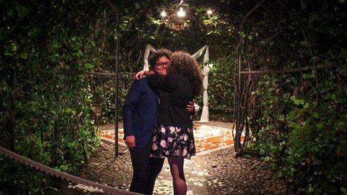 Couple embracing amidst plants at night